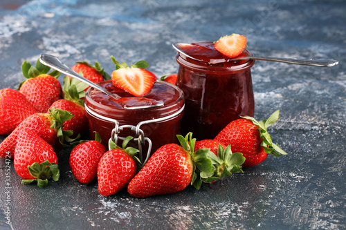 Strawberry jam in a glass jar with strawberries and leaves on rustic background. Homemade strawberry marmelade or jam