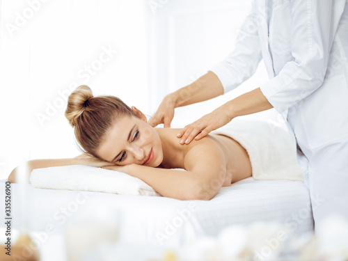 Young and blonde woman enjoying massage of back in spa salon. Beauty concept