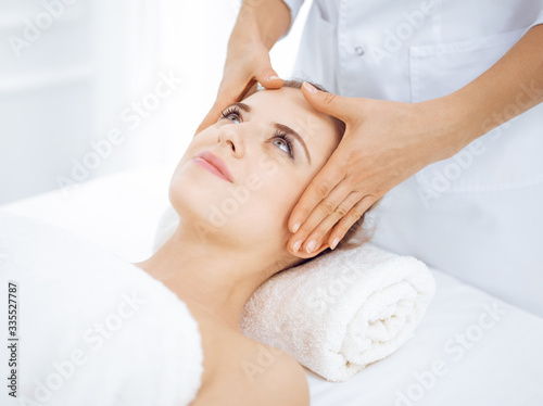 Young and blonde woman enjoying facial massage in spa salon. Beauty concept