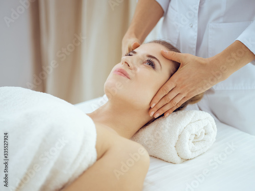 Young and blonde woman enjoying facial massage in spa salon. Beauty concept