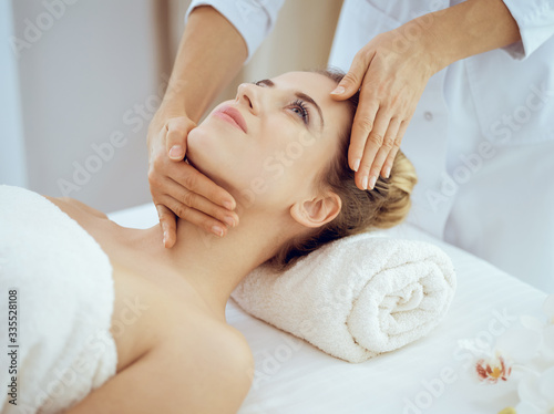 Young and blonde woman enjoying facial massage in spa salon. Beauty concept