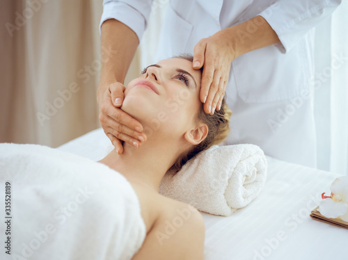 Young and blonde woman enjoying facial massage in spa salon. Beauty concept