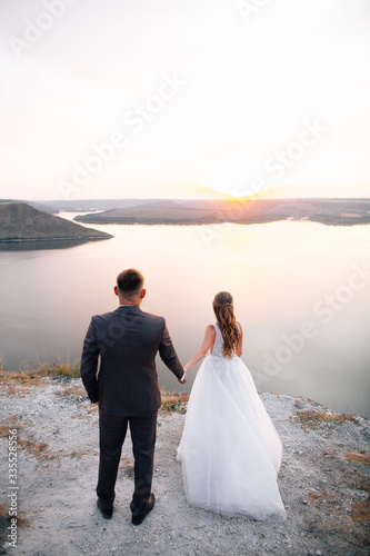 Bride holding grooms hands each others hands and looking at sunset. Outdoor engagement concept.