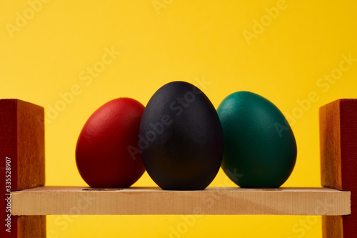 Colored black green blue red easter eggs on bright yellow background