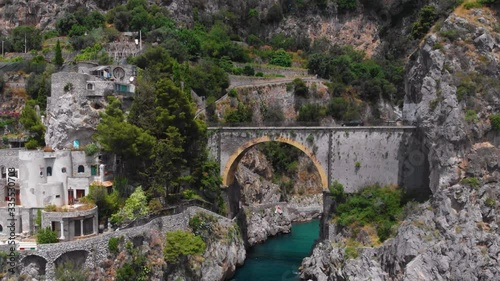 Aerial view inside bay of Fiordo di furore beach. Incredible beauty panorama of a mountains paradise. The rocky seashore of southern Italy. Sunny day. Stone bridge traffic, cars and motorcycle. Amalfi