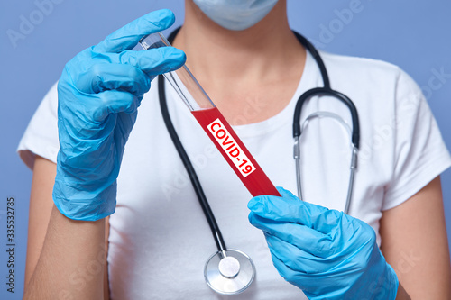 feceless portrait of doctor analyzes tubes of blood in lab, medical staff checked sample at hospital, lady wearing white shirt and disposable gloves, posing isolated over blue studio background.