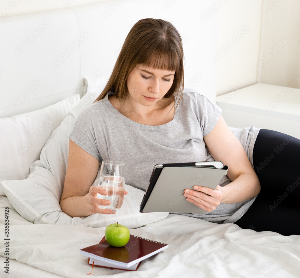 Young beautiful girl with tablet is studying at home in bed Young beautiful girl with tablet is studying at home in bed