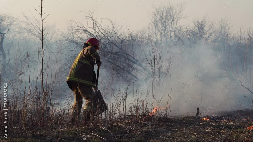 Firefighter puts out a forest fire near the city. Burning grass with