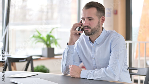 Serious Young Man Talking on Smartphone in Office