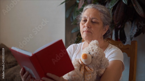 Quarantine senior woman reading book rest with teddy bear toy. Home isolation. 