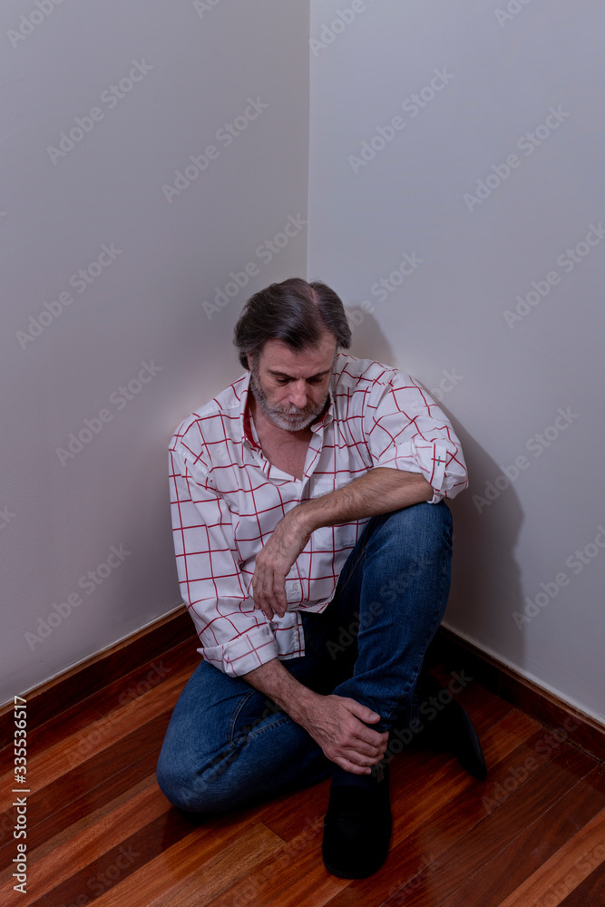 Mature man, alone and depressed, with a careless beard, is sitting in the corner of a room
Mature man, alone and depressed, with a careless beard, is sitting in the corner of a room