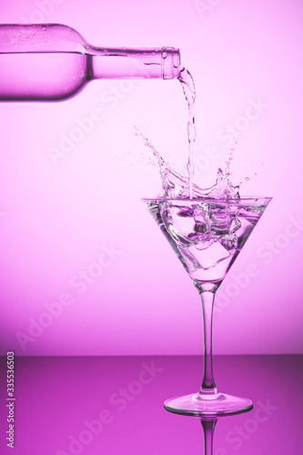 Pink bottle spilling liquid into a cocktail glass and making splash. Pink background  alcoholic drinks and cocktails concept.