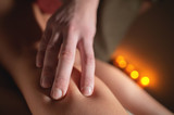 Close-up hand of a massage therapist massaging the legs of a female client against the background of burning candles in an office with a cozy light.