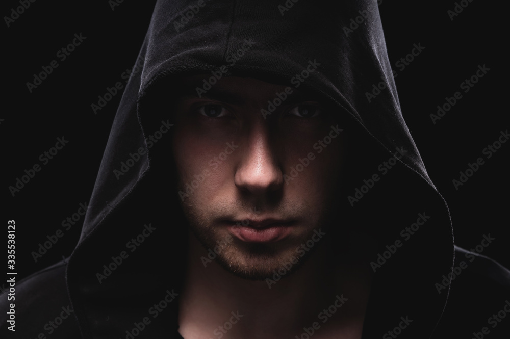 Close-up portrait of a courageous man in a deep dark hood on a black background. The concept of secrecy of secrets and people hiding from the government. Hackers and thieves. Low key Close-up portrait of a courageous man in a deep dark hood on a black background. The concept of secrecy of secrets and people hiding from the government. Hackers and thieves. Low key