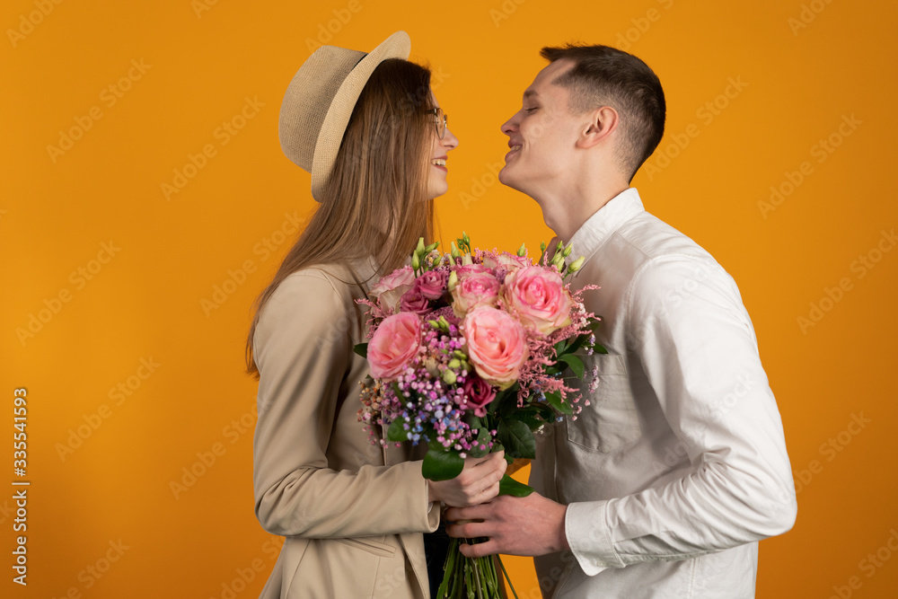 Side view of smiling couple with flowers looking at each other isolated on yellow background Side view of smiling couple with flowers looking at each other isolated on yellow background