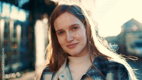 Portrait of cheereful dreming young redhair woman looking at camera, posing outdoor in downtown street. Female portrait. Rays of the sun photo