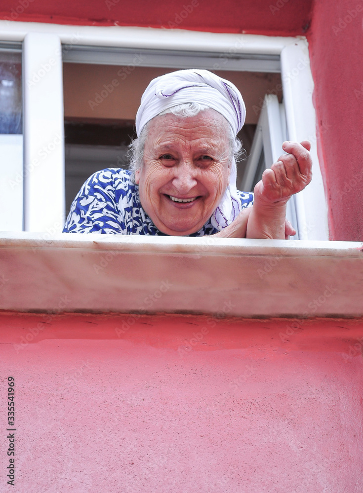 © berna_namoglu - Senior woman leaning on window in her apartment