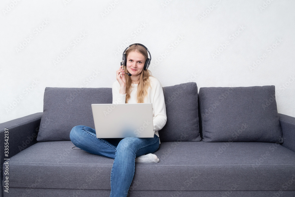 Caucasian woman working home sitting on a sofa with a laptop and a headphones on the white background. Stay home, quarantine concept Caucasian woman working home sitting on a sofa with a laptop and a headphones on the white background. Stay home, quarantine concept