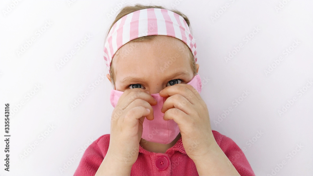 Little girl in headband wearing protective pink fabric mask against coronavirus COVID-19 pandemic white background.Wuhan virus epidemic quarantine. Child touching face, handmade sewn protection mask. Little girl in headband wearing protective pink fabric mask against coronavirus COVID-19 pandemic white background.Wuhan virus epidemic quarantine. Child touching face, handmade sewn protection mask.