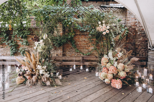 Wedding decorations. The wedding ceremony area in the loft against a brick wall is decorated with compositions of flowers and greenery, candles and dried flowers
