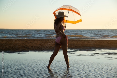 Silhoutte of a pretty senior Asian female in a swimming suit standing and hold umbrella posing on the beach..