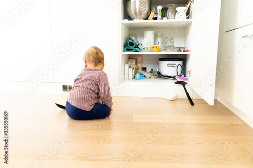 Toddler making mess in kitchen. Infant plays and discovers kitchen utensils. Babys and kids make chaos in the living space. Baby mess in cabinet. Open cabinet. Baselland, Switzerland - 03.04.2020