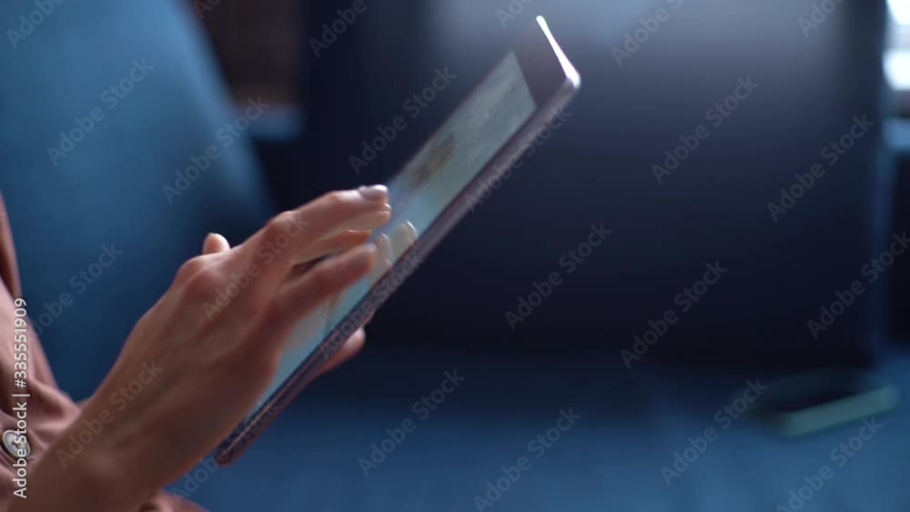 Woman touching screen of digital tablet, hands of close-up. Female sitting on cozy couch with gadget in the living room. Concept of internet research. Tracking shot in slow motion.