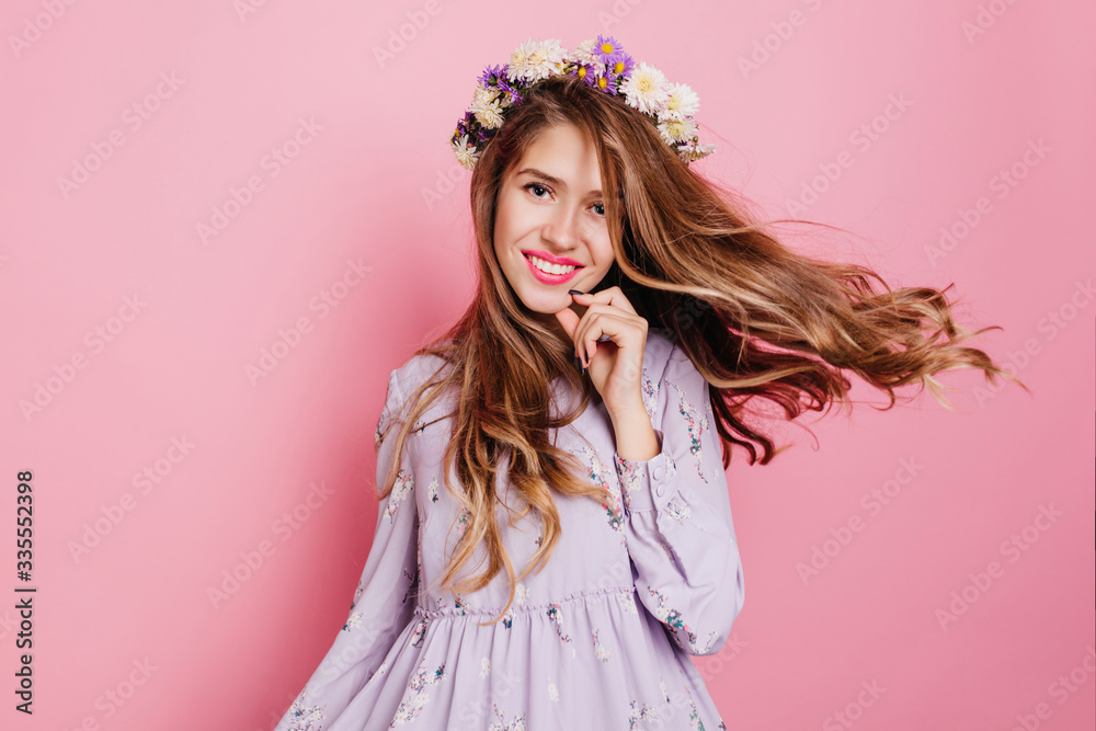 Smiling girl with wavy hair wearing circlet of colorful flowers. Indoor photo of dancing glad woman in romantic dress.