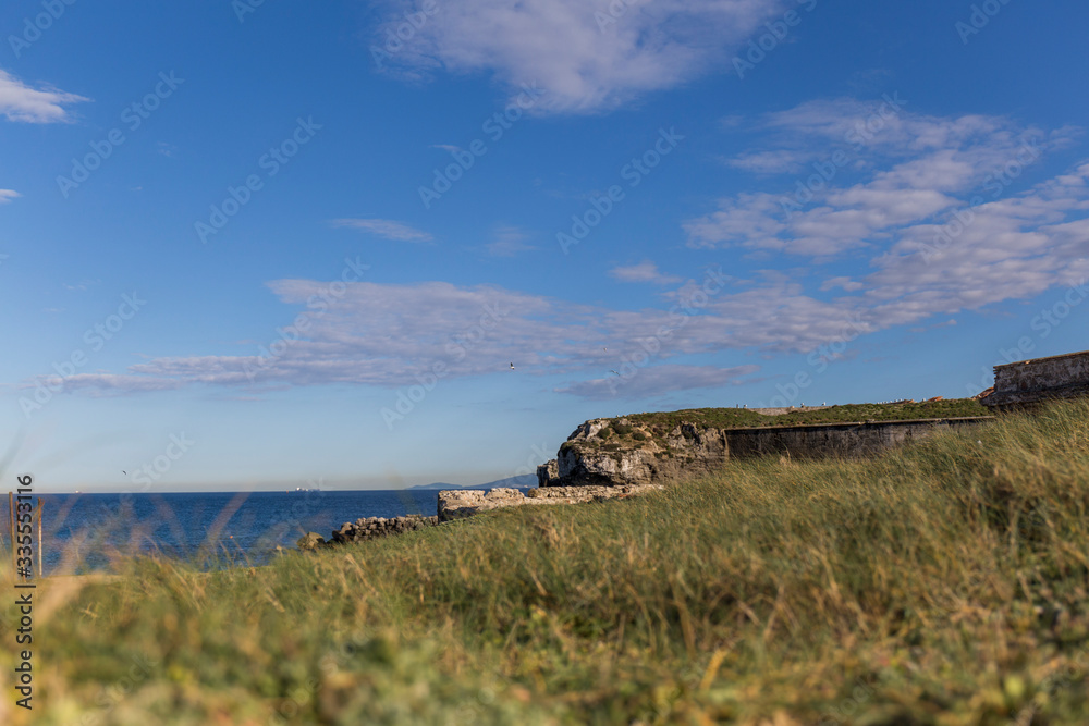 from a grassy hill we see the coastal landscape, blue sea and clear sky