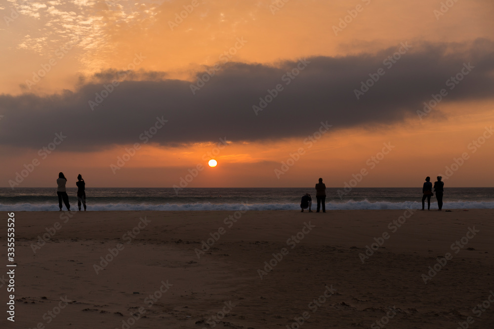 sunset on the beach, sky with orange colors and clouds, sea with small waves