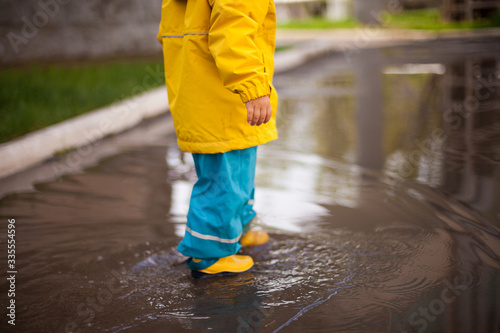 little feet of a child in rubber boots and a waterproof suit walk on the water.