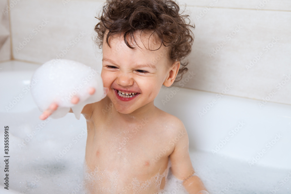 Happy baby washes in the bath holds foam in his hands and rejoices. emotional baby. hygiene procedures Happy baby washes in the bath holds foam in his hands and rejoices. emotional baby. hygiene procedures
