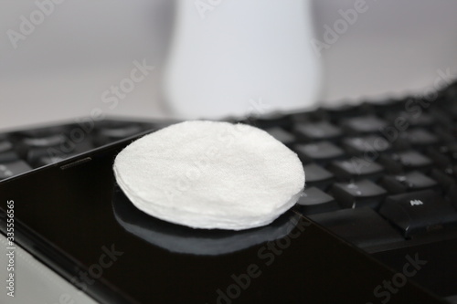 Round pledget / swab on smartphone screen and compuer keyboard close up, in background white pharmaceutical bottle with cleaning liquid photo