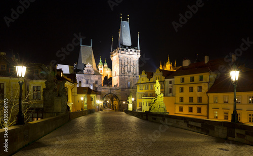 Night colorful Prague gothic Castle with St. Nicholas' Cathedral and Bridge Tower from Charles Bridge with its baroque Statues without People at the time of Coronavirus, Czech Republic