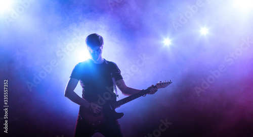 Young male singer performing on a stage and playing the guitar. Smoky blue background