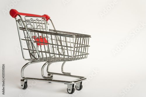 Empty supermarket consumer food trolley from steel with red plastic handle on a gray background with empty space © Sea_Inside_Soul