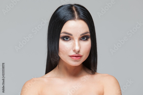 Closeup of beautiful woman face with beauty makeup and long brunette hair looking at camera isolated on grey background