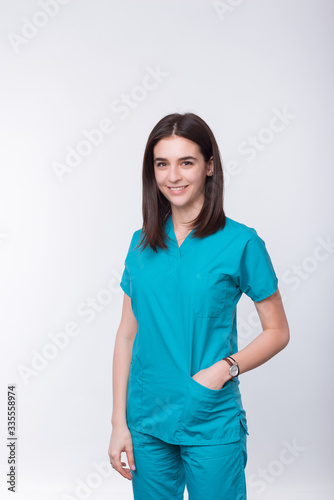 Vertical portrait of a young smiling medical student or female doctor holding hand in pocket on white background.