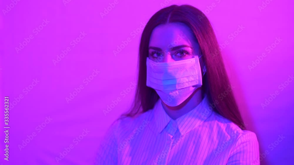 Portrait of a beautiful business woman with gray eyes wearing a protective mask. Young girl standing on a background in bright multi-colored neon colors. Coronavirus, Covid-19, global problem. Portrait of a beautiful business woman with gray eyes wearing a protective mask. Young girl standing on a background in bright multi-colored neon colors. Coronavirus, Covid-19, global problem.