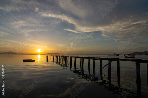 Landscape reflection of wooden bridge on sea in early morning at fisherman pier Jelutong, Penang. Penang Bridge at background.