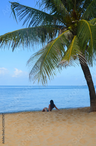 Young girl rear view sitting on the shore of a sandy beach and looking at the sea and meditating