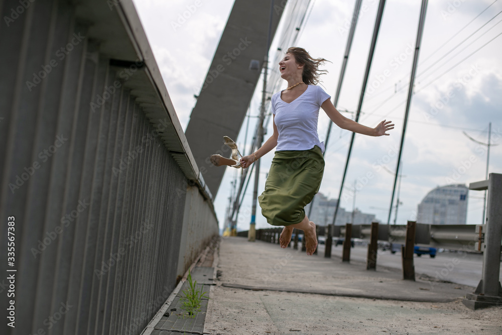 horizontal photo of a slender girl in a white t-shirt and green skirt on the background of the bridge