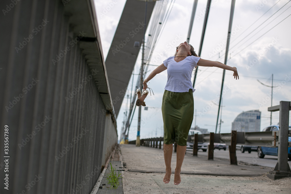 horizontal photo of a slender young girl in a white t-shirt and green skirt on the background of the bridge