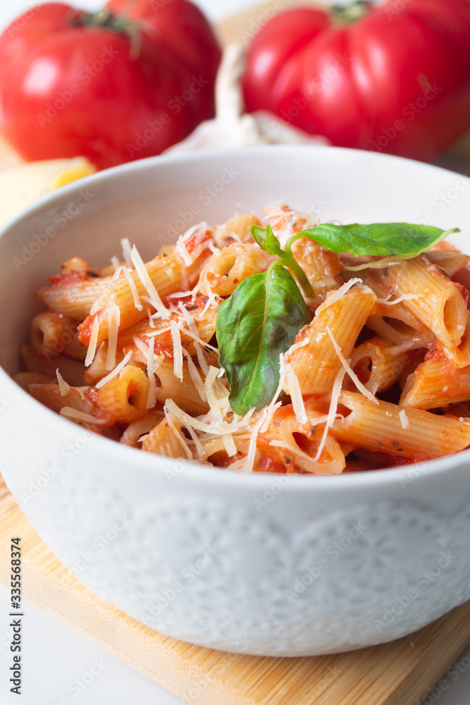 Classic italian penne pasta arabiata with its ingredients in the background: fresh tomatoes, basil, garlic and parmesan cheese Classic italian penne pasta arabiata with its ingredients in the background: fresh tomatoes, basil, garlic and parmesan cheese