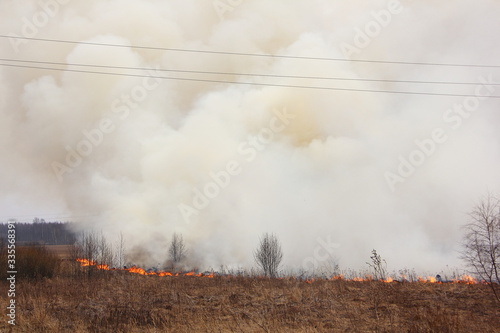 Big smoke cloud on burning dry grass field under the high voltage wires, air power line destruction damage