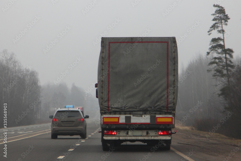 Suburban road traffic, a car overtakes a slow truck in the fog with limited visibility at misty spring day