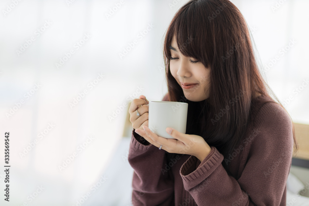 Asian woman smiling and holding cup of coffee in her bedroom. corovavirus covid-19, stay at home, work form home concept. Asian woman smiling and holding cup of coffee in her bedroom. corovavirus covid-19, stay at home, work form home concept.