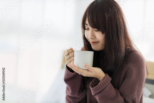 Asian woman smiling and holding cup of coffee in her bedroom. corovavirus covid-19  stay at home  work form home concept.