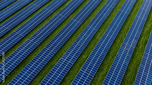 Aerial drone photo of a photovoltaic solar cell farm. Dark blue solar panels against a contrasting green grass field.