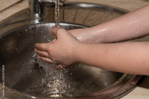 A child washing hands in kitchen at home, quarantine.